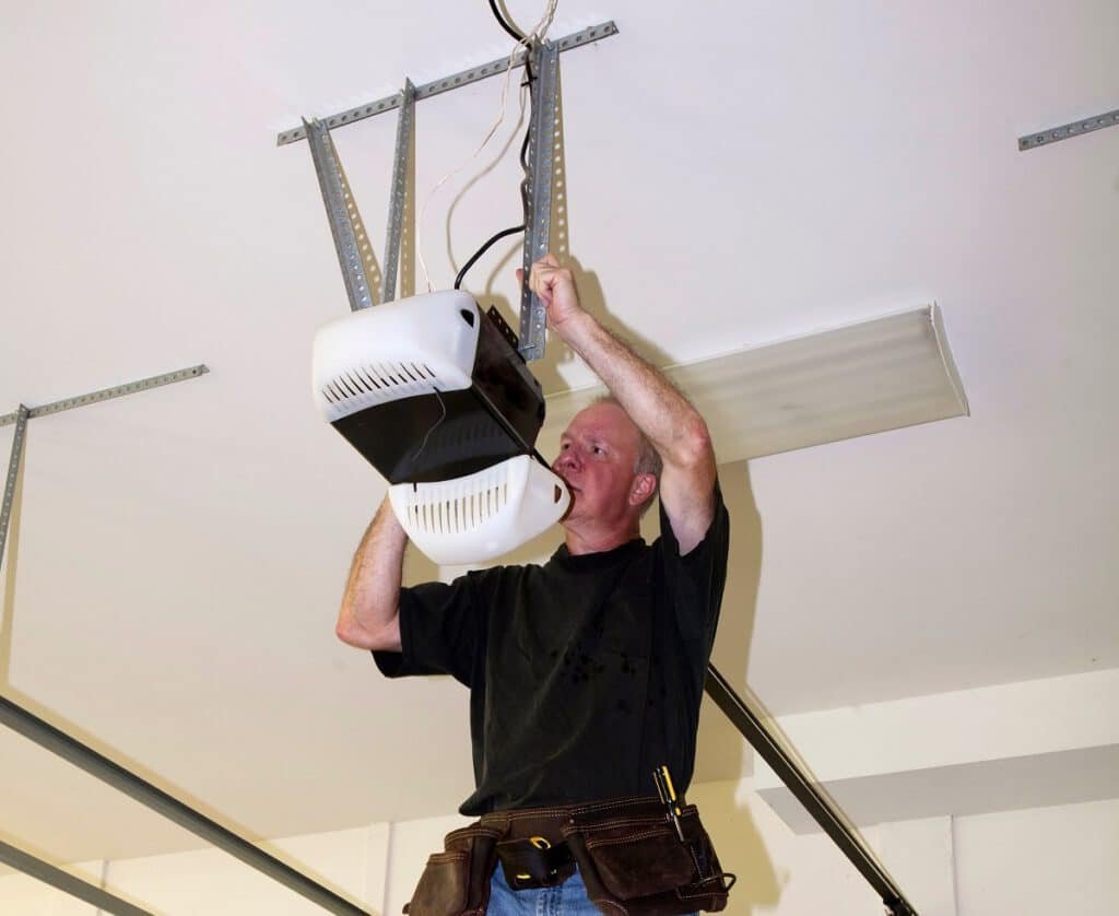 Man standing on a ladder fixing a mechanical garage door opener